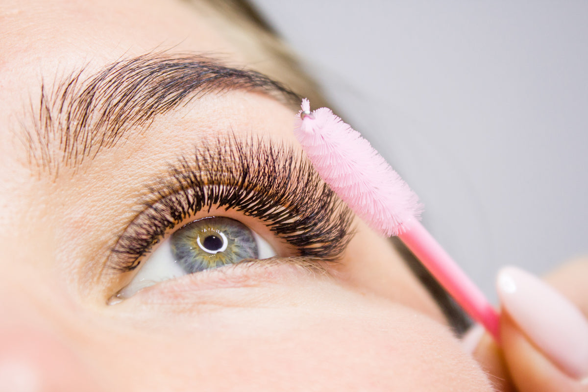 Woman using a spoolie to brush lashes for lash aftercare. Cartel Lash