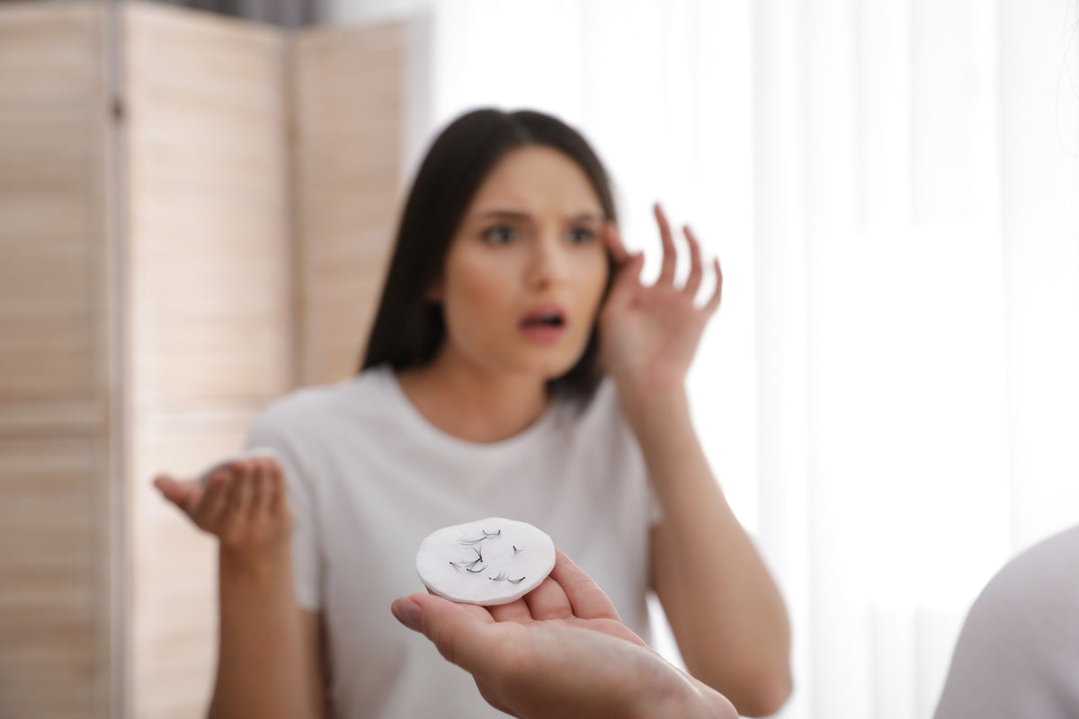 Woman holding cotton pad with fallen lash extensions. Cartel Lash
