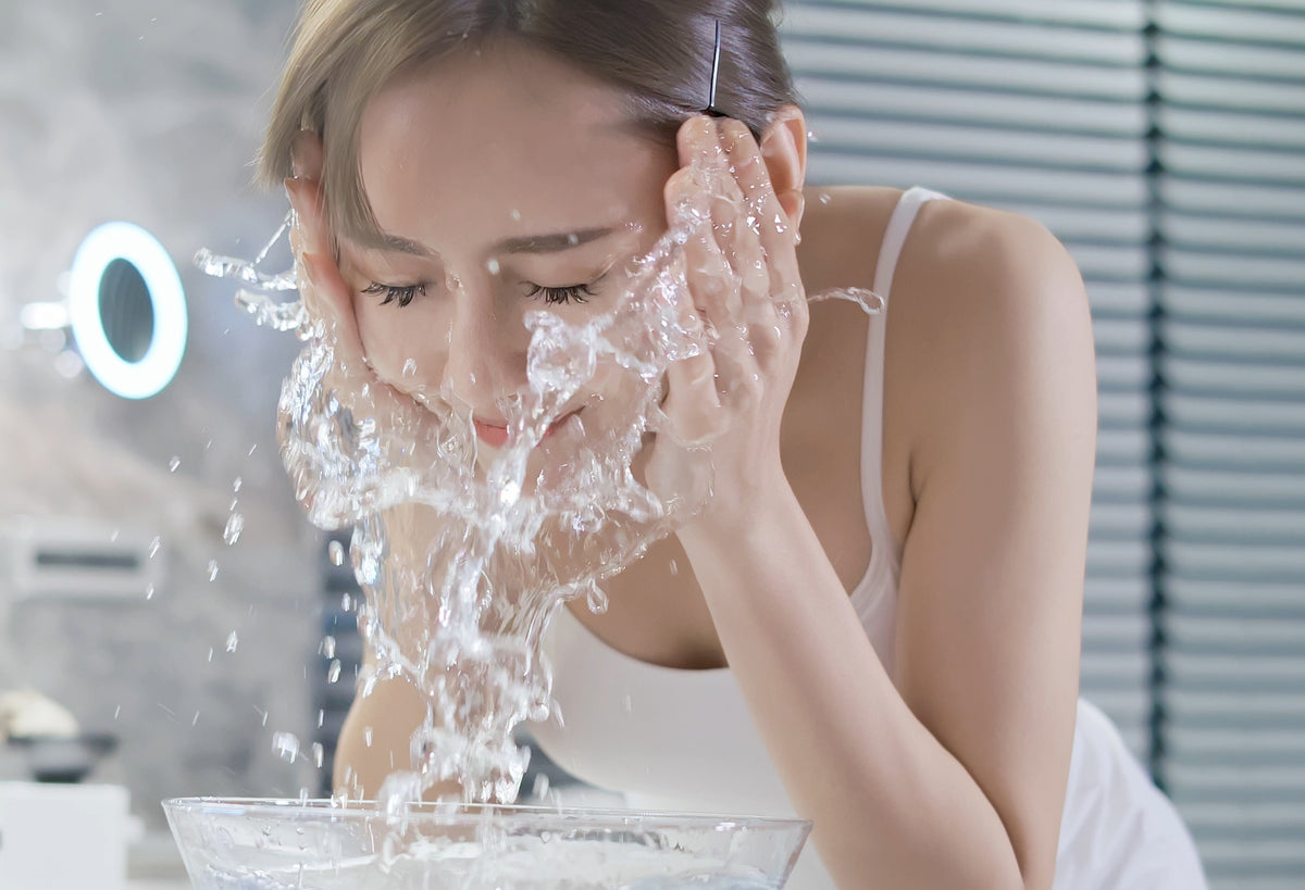 Woman prepping her face and lash extensions to clean by splashing water on it from a bowl. Cartel Lash