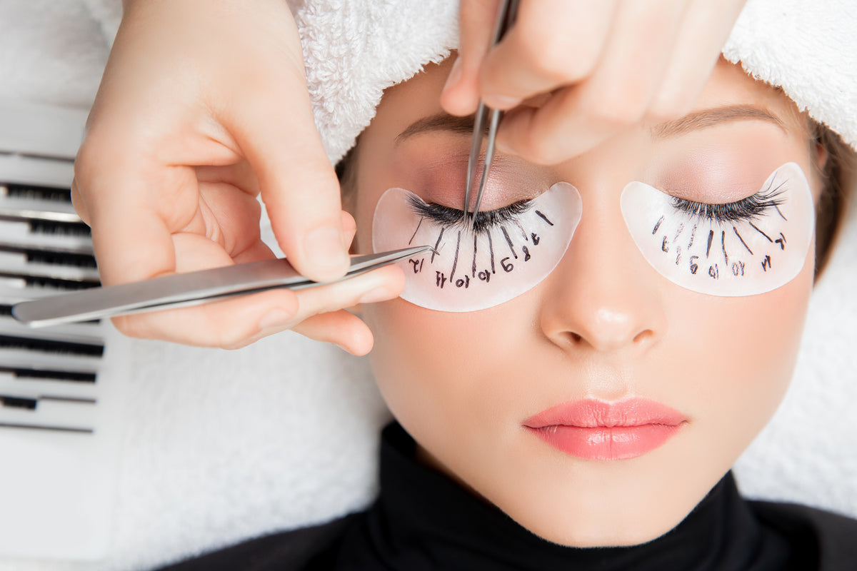 Woman getting eyelash extension procedure. Lash tech using two lash tweezers to isolate. Cartel Lash