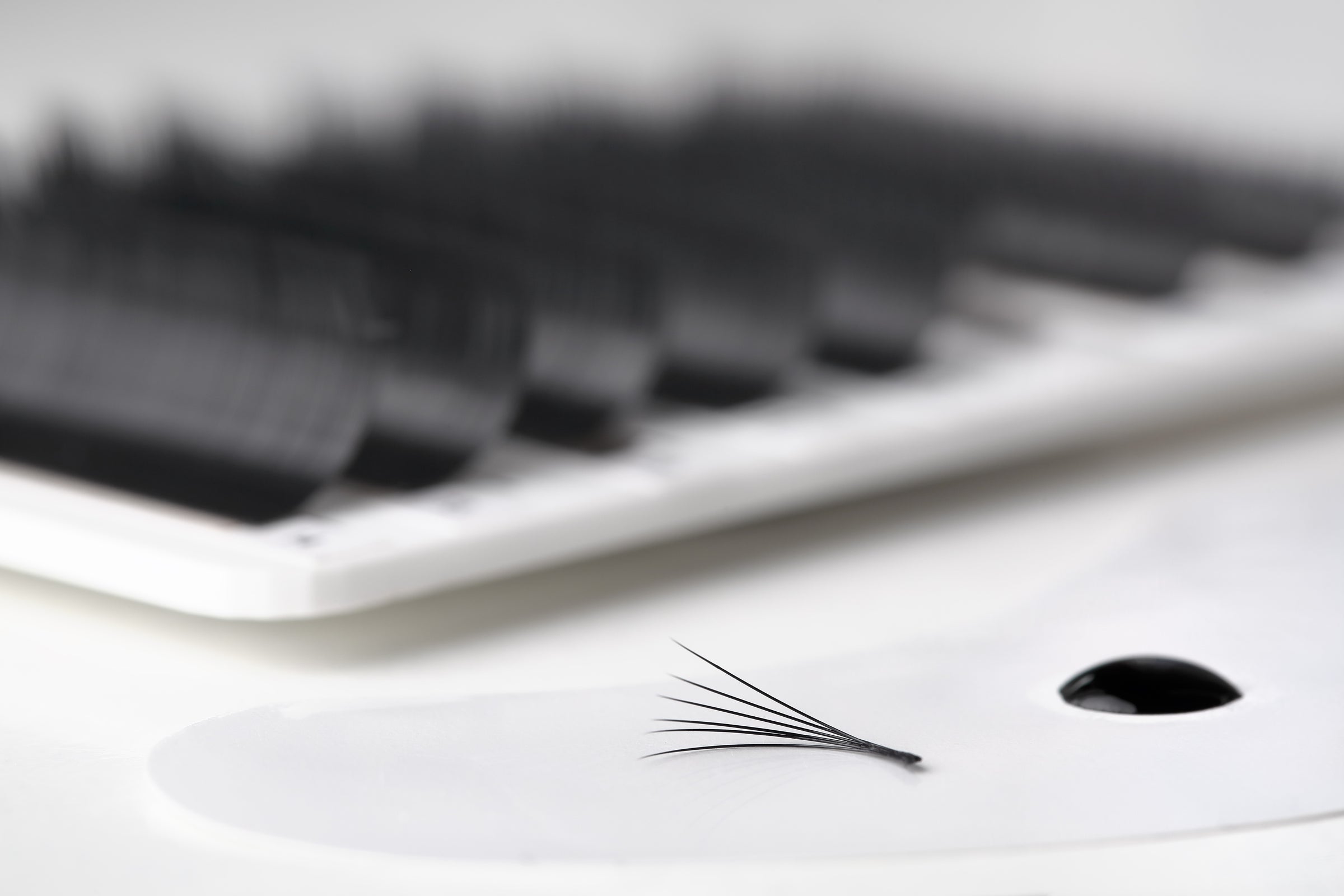 Drop of eyelash glue with eyelash extension and lash tray in the blurred background. Cartel Lash