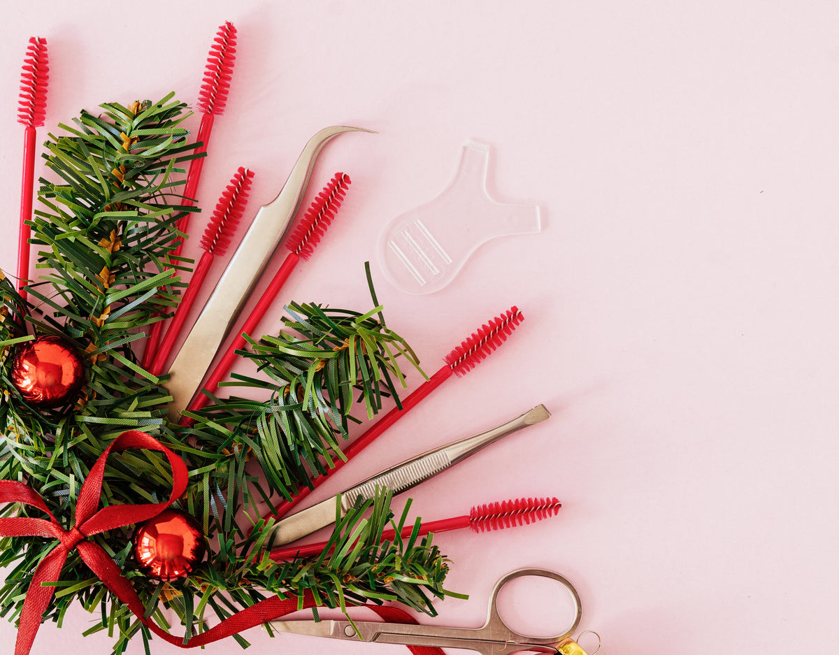 Lash tweezers, spoolie and tools for eyelash extensions on the left side with a Christmas theme. 