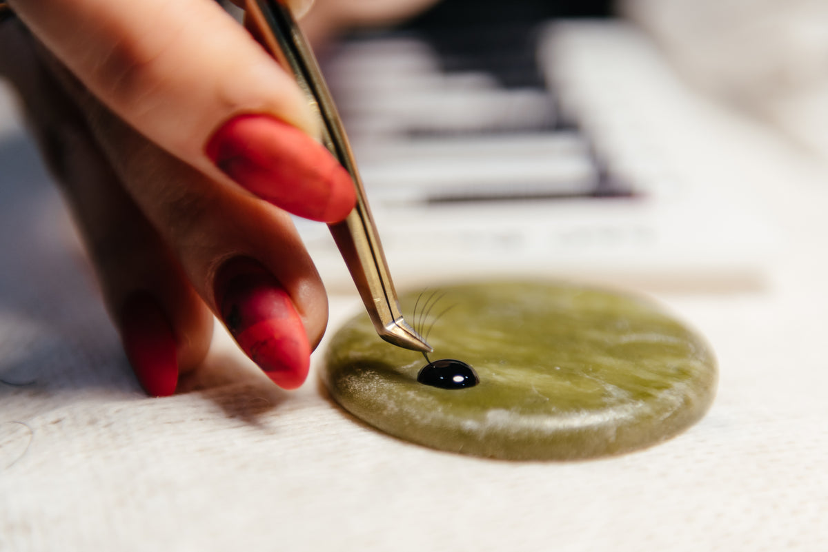 Eyelash Extension tweezer dipping into lash adhesive. Cartel Lash.