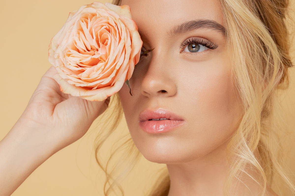 Woman holding an orange flower next to her natural lash extensions. Cartel Lash