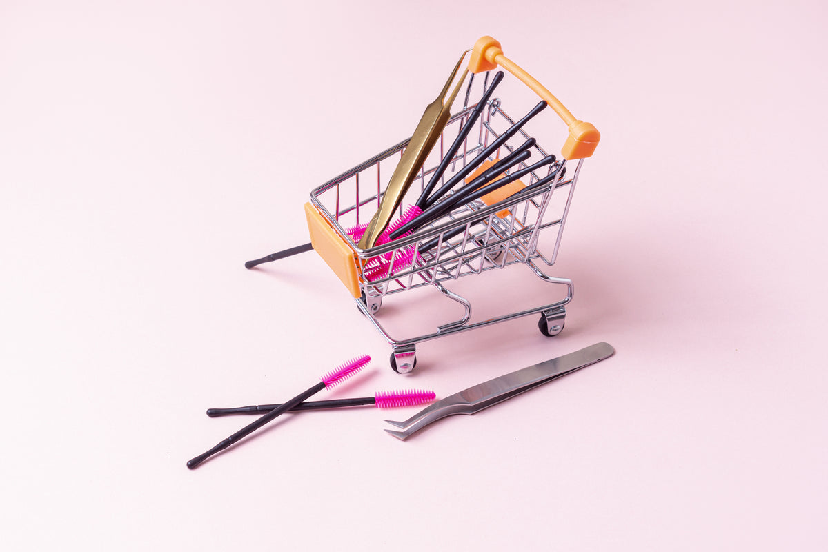 Shopping cart with lash tweezers and lash brush for eyelash extensions on pink background. 