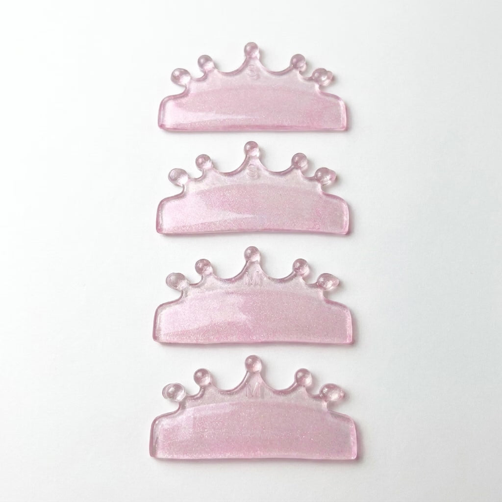 Four pink glitter crown-shaped lash lift shields arranged vertically on a plain white background