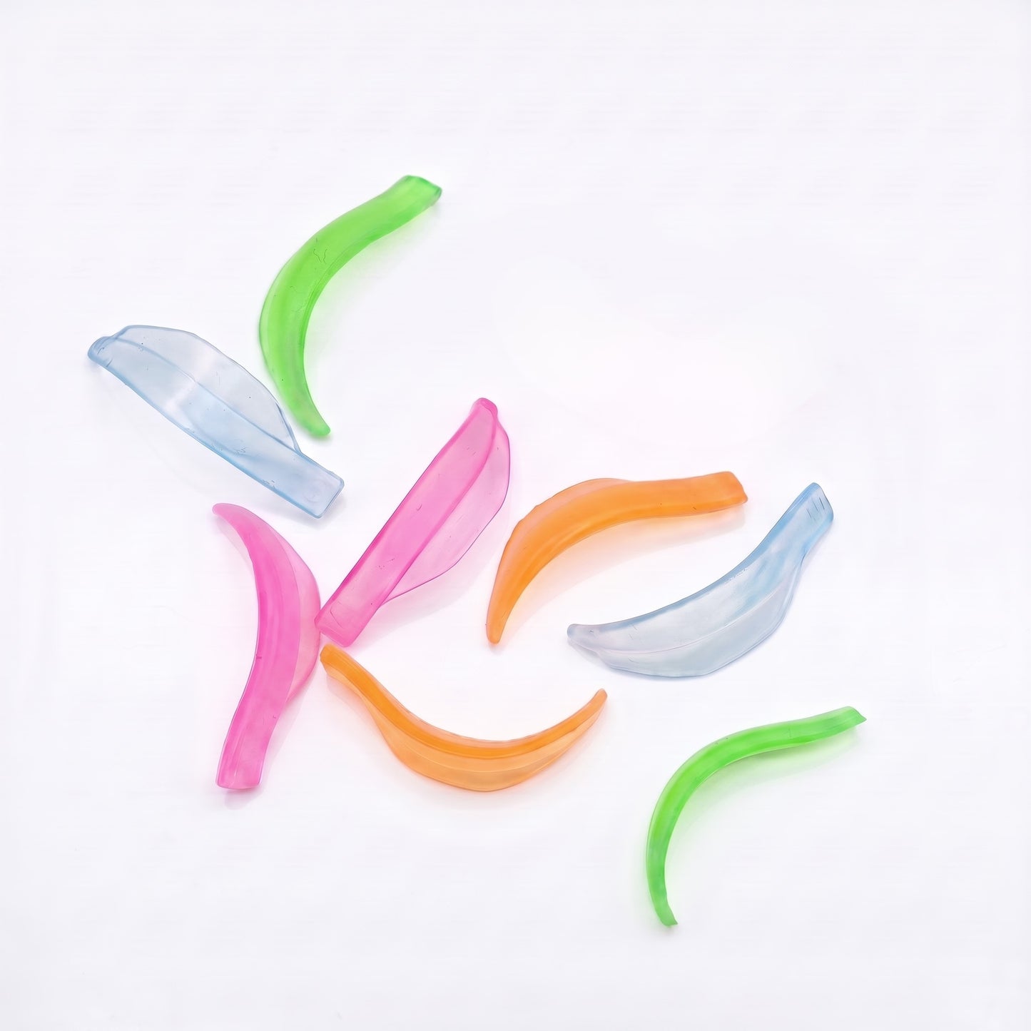 Six translucent silicone lash lift sheilds in pink, orange, green, and light blue, scattered on a plain white background.